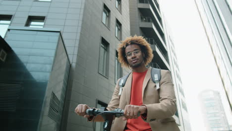 Portrait-of-Cheerful-African-American-Man-Standing-with-E-Scooter-in-City